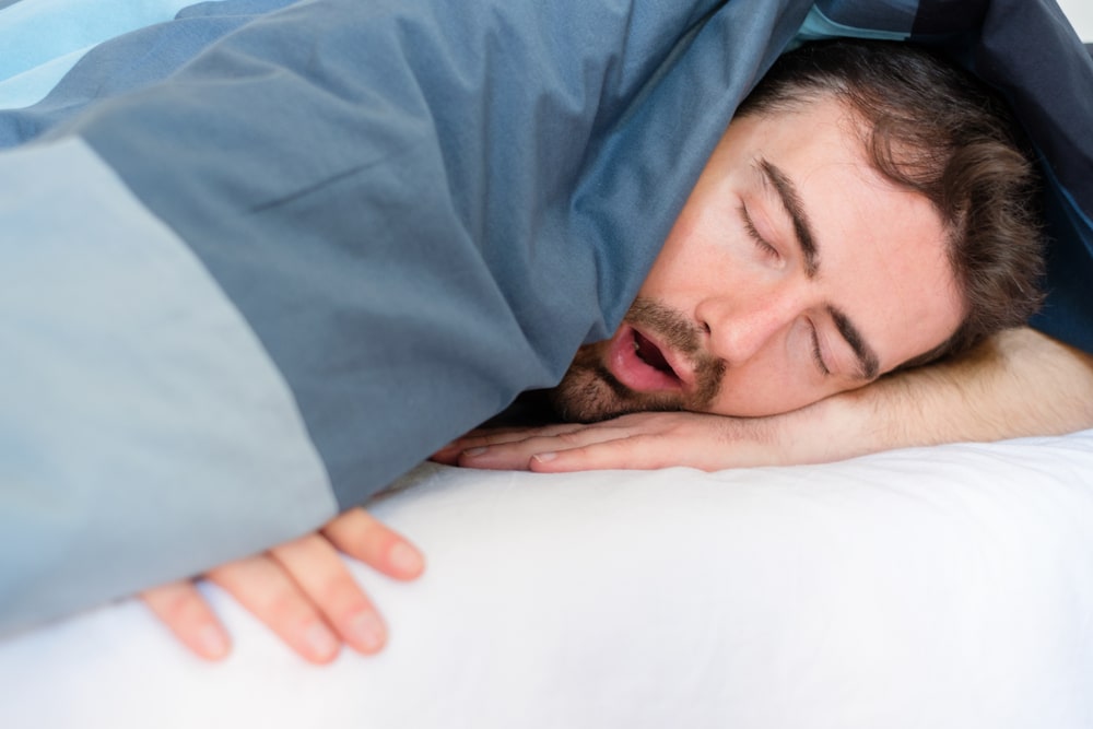 Man snores loudly in bed, getting disruptive sleep that will leave him drowsy in the morning.