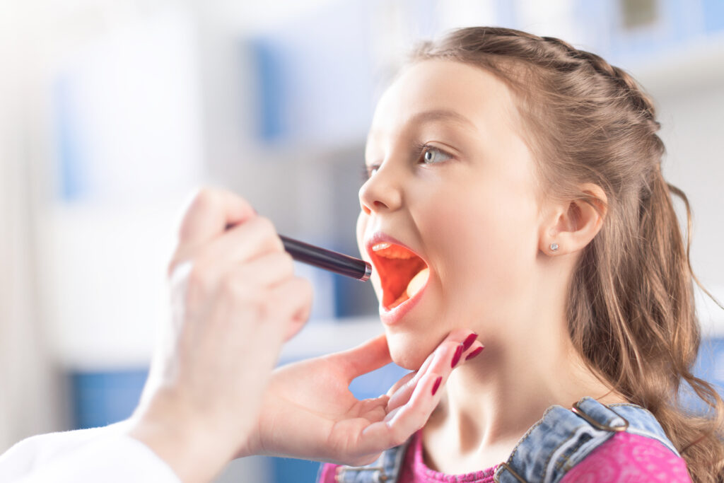 Doctor looks down a child's throat to inspect her tonsils