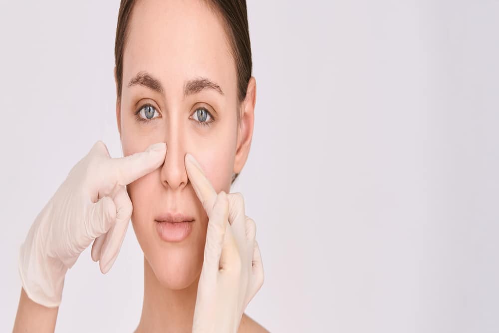 Gloved doctor's hands holds woman's nose ahead of septoplasty