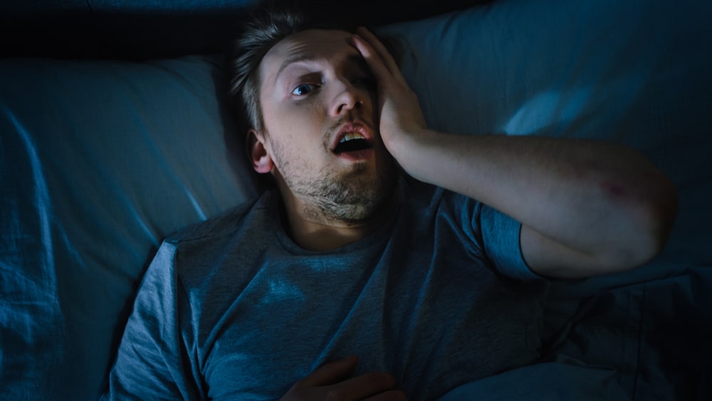 Man looks uncomfortable in bed - his allergy symptoms are preventing him from sleeping.