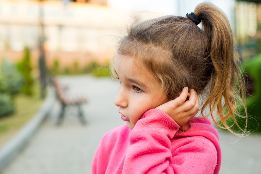 Young girl wearing pink holds her ear due to pain from an ear infection.