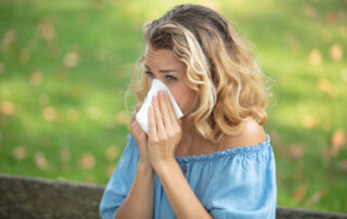 Woman blows her nose into a tissue, wondering whether her symptoms are related to allergies