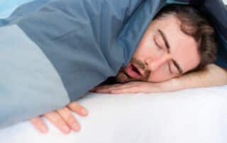 Man snores loudly in bed, getting disruptive sleep that will leave him drowsy in the morning.